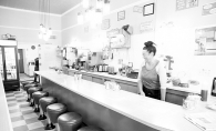 A waitress stands behind the bar area at Not Justa Cafe in this black and white photo