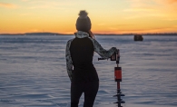 Standing with an ice auger on frozen lake