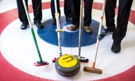 Curlers at the St. Croix Curling Center hold their brushes near a stone.