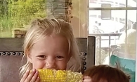 Two children smile while eating sweet corn in this Lens on St. Croix Valley winning photograph.