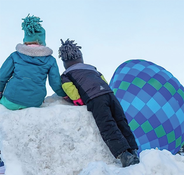 Children on a snow hill watch balloons at the Hudson Hot Air Affair 2020