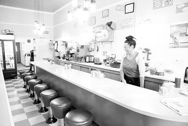A waitress stands behind the bar area at Not Justa Cafe in this black and white photo