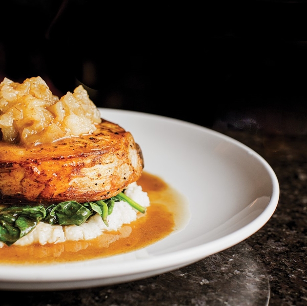 Pork Chop with cheddar grits, greens, smoked applesauce and cider jus.
