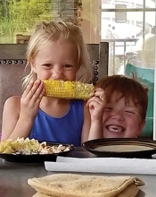 Two children smile while eating sweet corn in this Lens on St. Croix Valley winning photograph.