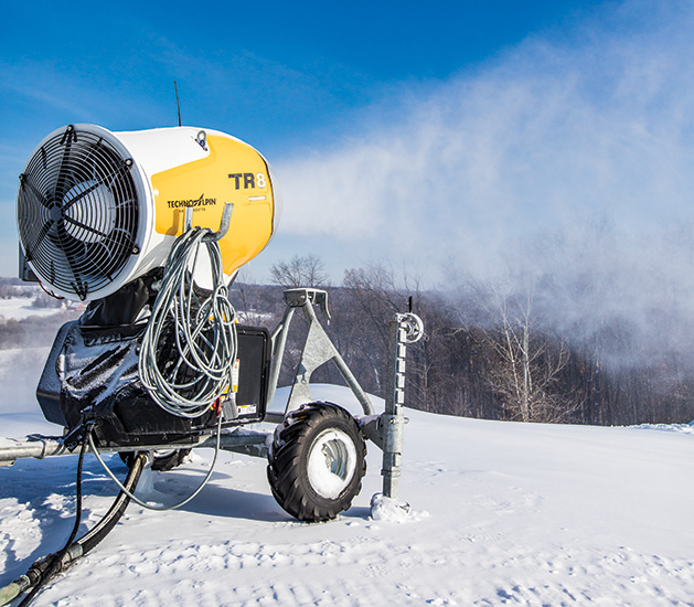 A snow machine blows snow onto a ski hill